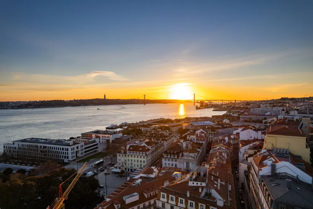 Sunset over the Tagus River in Lisbon with the 25 de Abril Bridge and Cristo Rei statue in the distance.